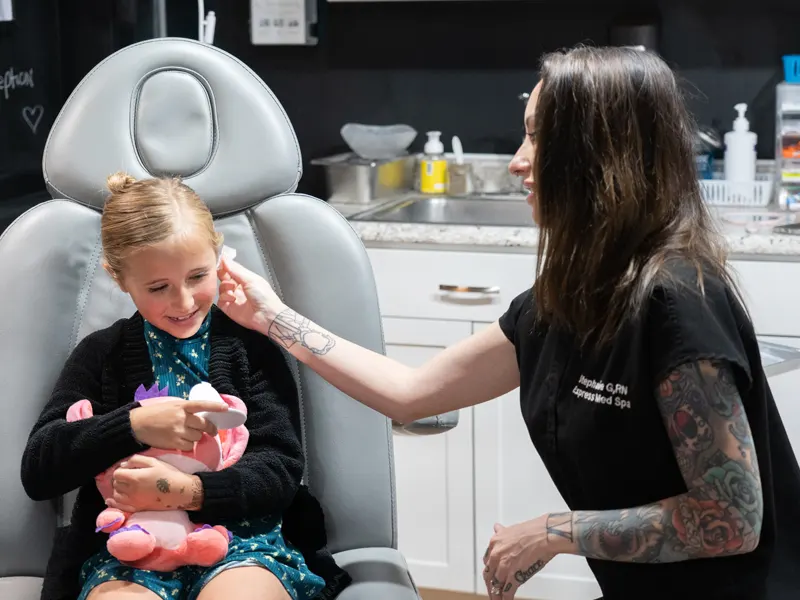 Smiling child comforted by a caring clinician during a gentle, safe ear piercing at Express Med Spa Frankfort.