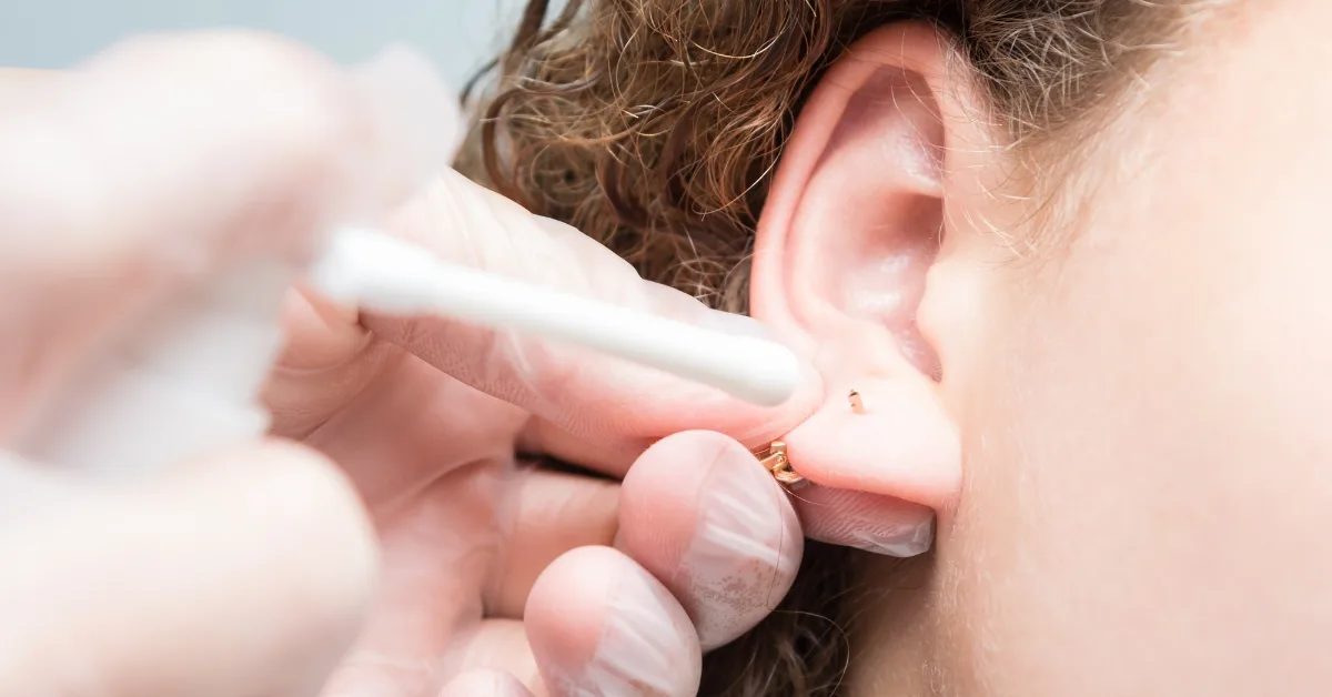 Person gently cleaning ear piercing with saline solution and gauze