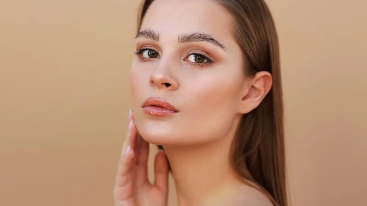 Woman with healthy, radiant skin touching her cheek, illustrating a daily vitamin C skincare routine