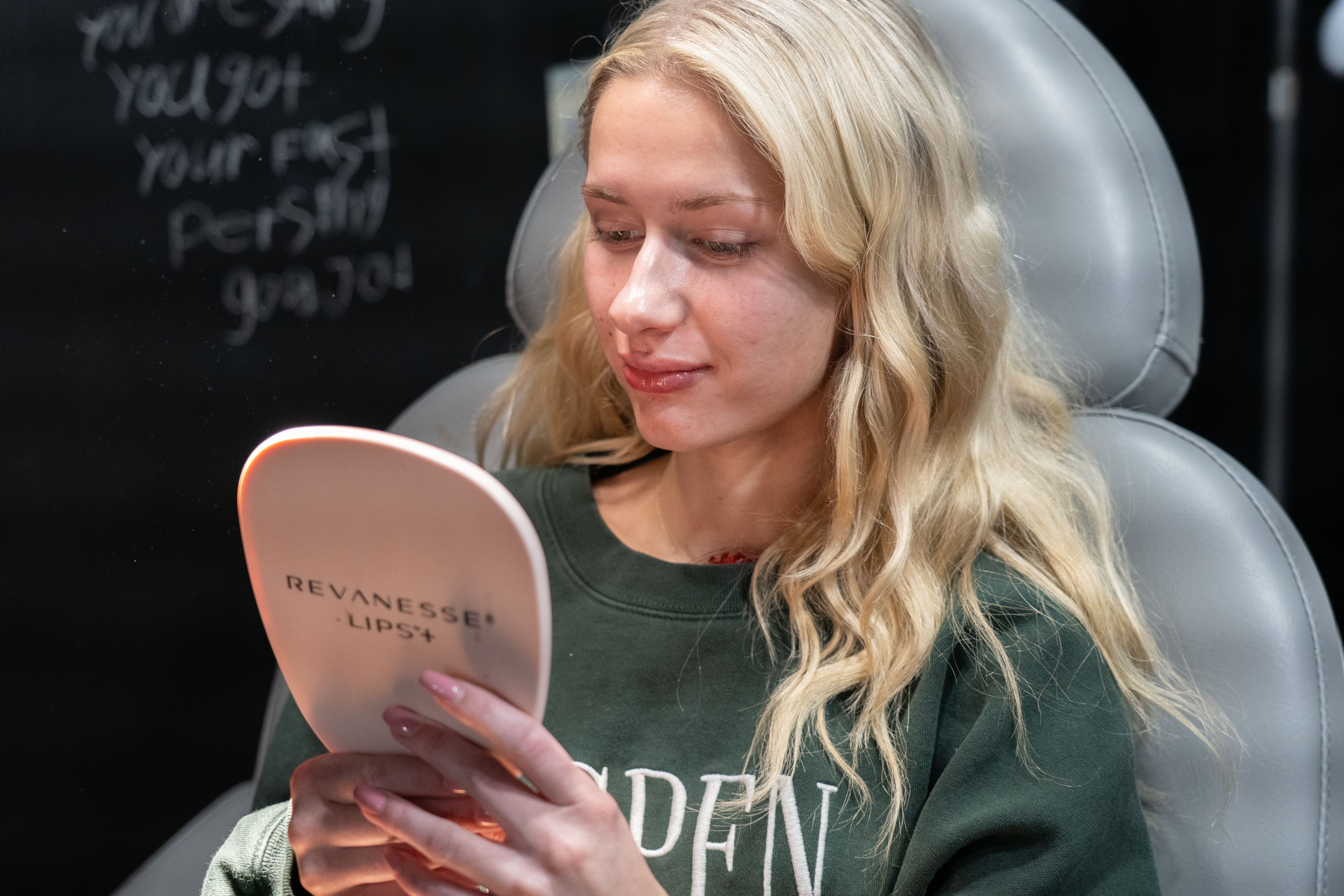 A client admires her enhanced lips after a Revanesse lip filler at Express Med Spa. Slight bruising visible, common post-treatment.